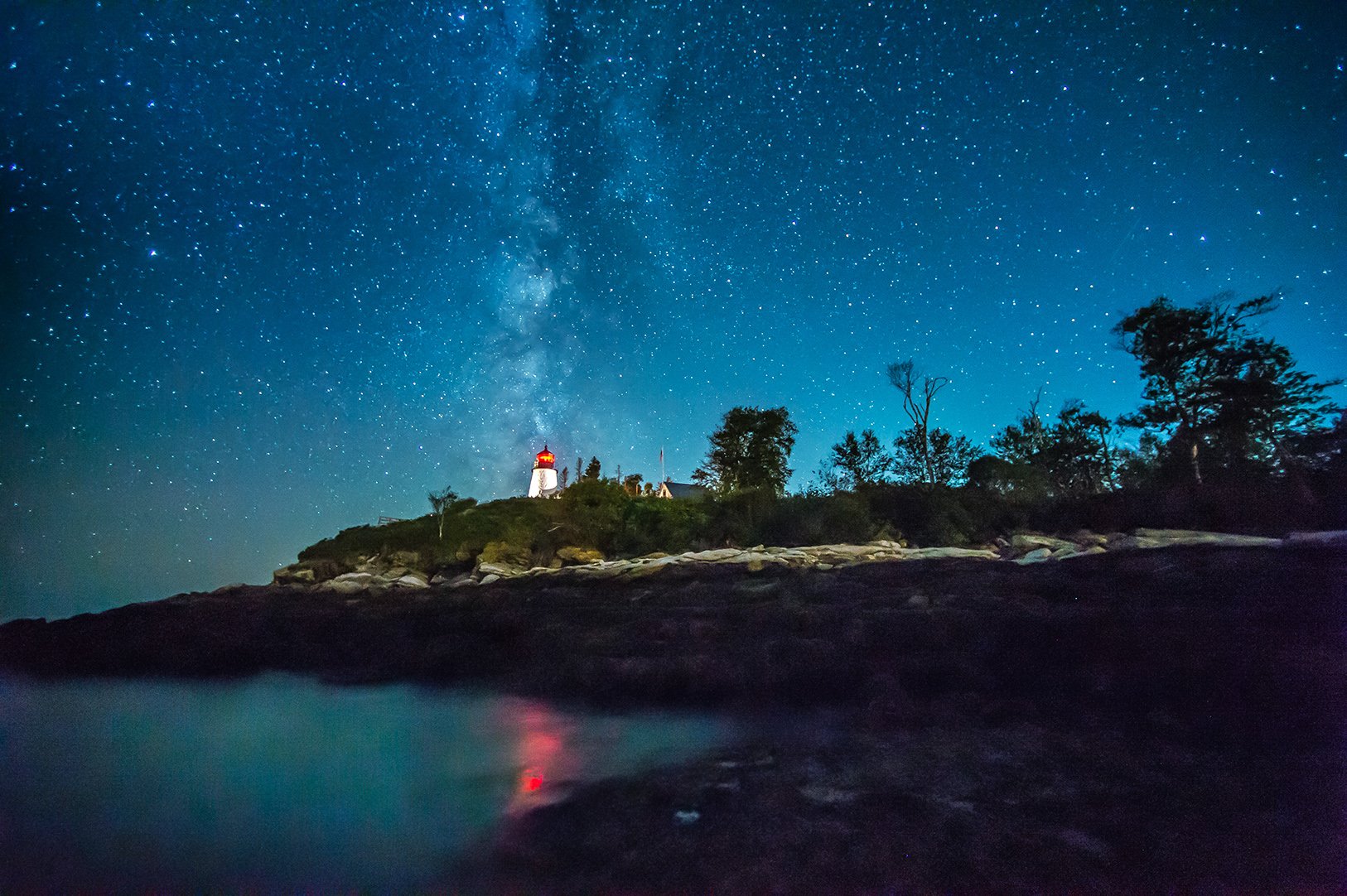 Maine's Burnt Island Lighthouse at night with reflection across water